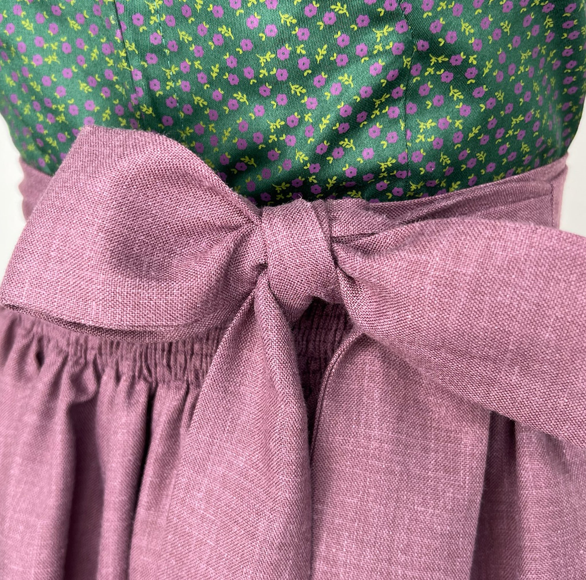 Rent this unique handmade green Versatile dirndl with a plum apron from our Munich collection. Perfect for Oktoberfest or elegant events. Available online or in-store.