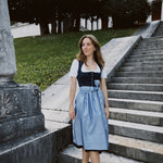 Apple of My Eye rental dirndl in Munich with deep blue jacquard floral bodice, silver buttons, and light blue pinstripe skirt—ideal for Oktoberfest dress hire.