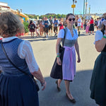 A woman in a traditional German dirndl with a lavender skirt and gray apron. Ready to rent a dirndl on Versatile OTM 