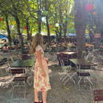 A woman wearing a traditional German Dirndl dress Berwin Wolf with a floral bodice and a light pink skirt stands in an outdoor Beergarden