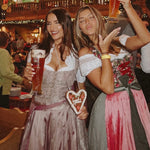 Coco Vero rented Dirndl for Oktoberfest rented on Versatile OTM. A pink premium rented Coco Vero Dirndl, woman wearing it in an Oktoberfest Tent with a friend wearing a Krüger Dirndl Dress rented on Versatile OTM