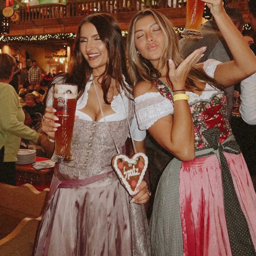 Coco Vero rented Dirndl for Oktoberfest rented on Versatile OTM. A pink premium rented Coco Vero Dirndl, woman wearing it in an Oktoberfest Tent with a friend wearing a Krüger Dirndl Dress rented on Versatile OTM