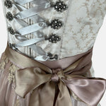 Close-up of a Krüger Dirndl featuring an ivory bodice with silver ribbon lacing and a gold embroidered apron. Skirt length 60cm. Elegant and luxurious.