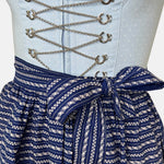Detail shot: Classic light blue and navy Krüger Dirndl with lace-trimmed neckline and patterned apron – available for rent via Versatile.