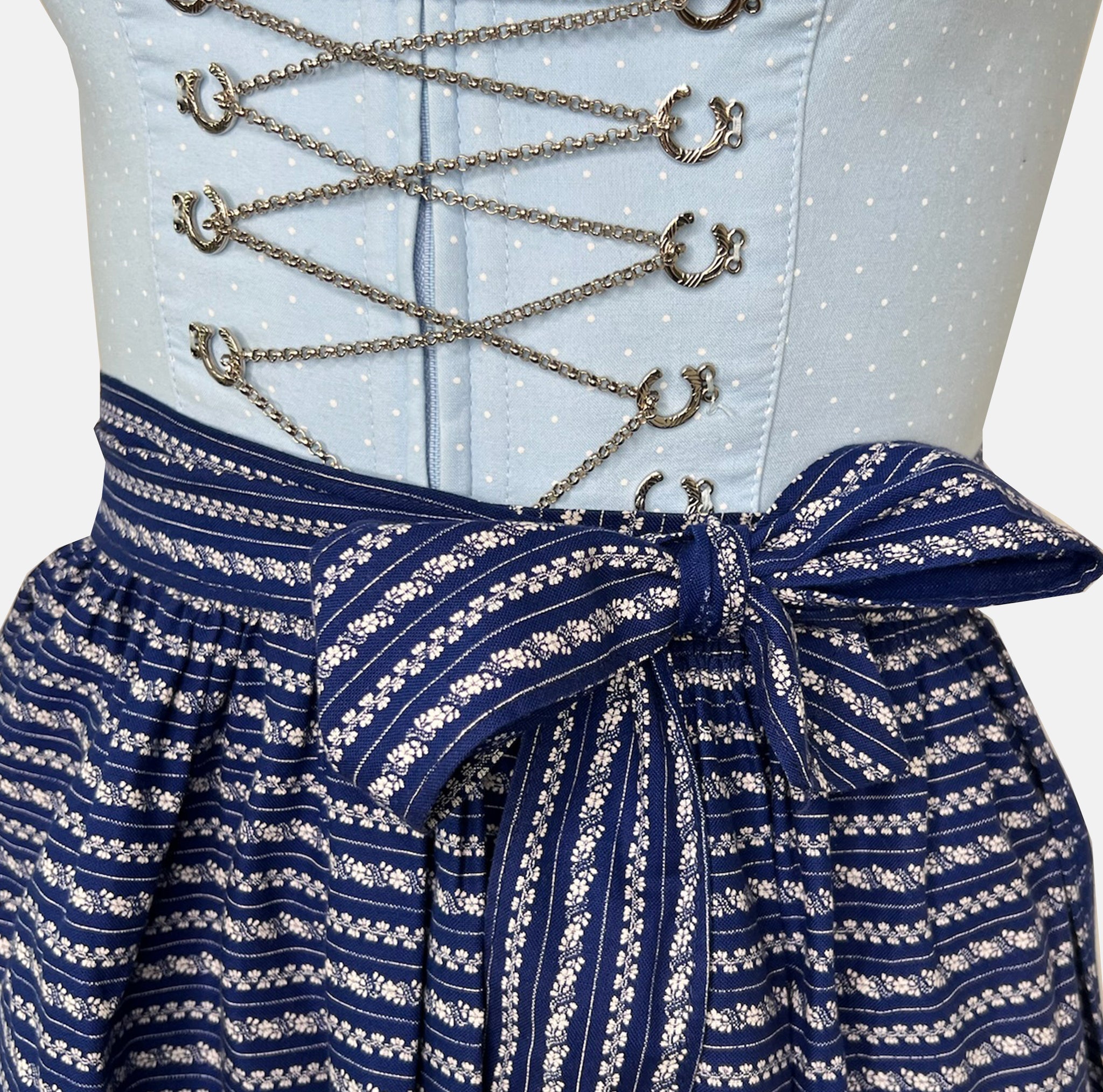 Detail shot: Classic light blue and navy Krüger Dirndl with lace-trimmed neckline and patterned apron – available for rent via Versatile.