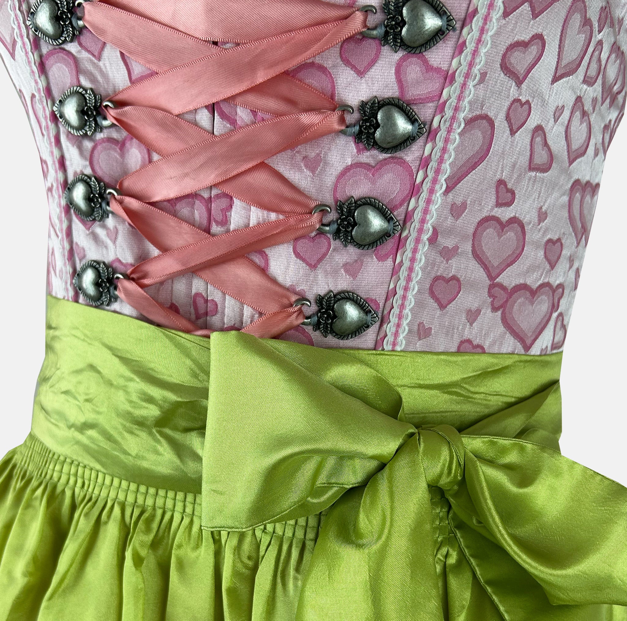 Krüger Madl dirndl with a pink heart-print bodice, green floral-trimmed apron, and pink gingham accents – playful and vibrant.