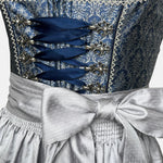 Elegant blue Krüger dirndl with silver apron, brocade bodice, and decorative lace details – available for rent at Versatile.