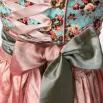 Krüger Madl Dirndl with aqua floral bodice, rosé satin skirt, green satin apron, and corset lacing. Mini 50 cm length—colorful and chic. Rent on Versatile!