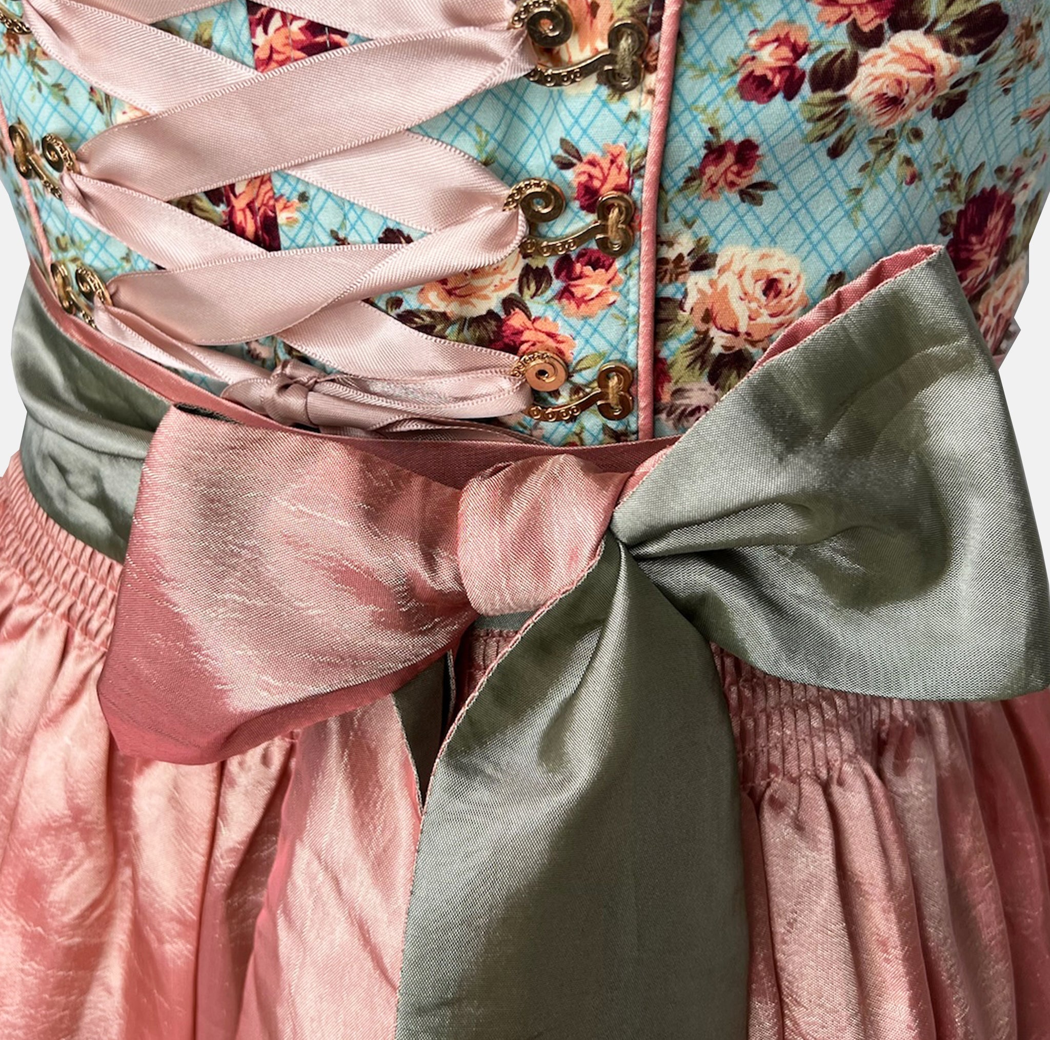 Krüger Madl Dirndl with aqua floral bodice, rosé satin skirt, green satin apron, and corset lacing. Mini 50 cm length—colorful and chic. Rent on Versatile!