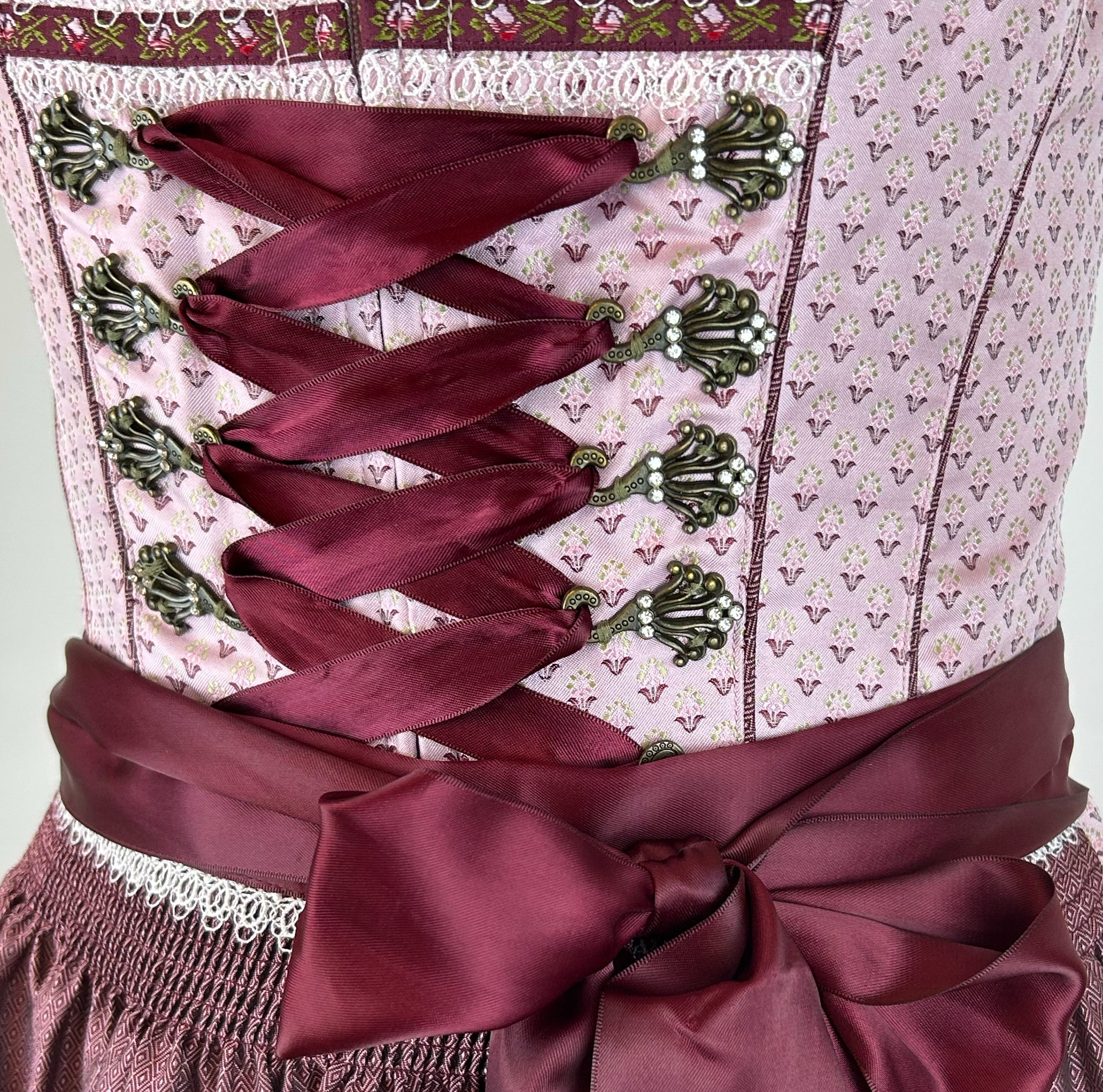 Elegant Krüger dirndl with pink bodice, burgundy lacing, and satin apron. Classic 60 cm length – available to rent in Munich or online.