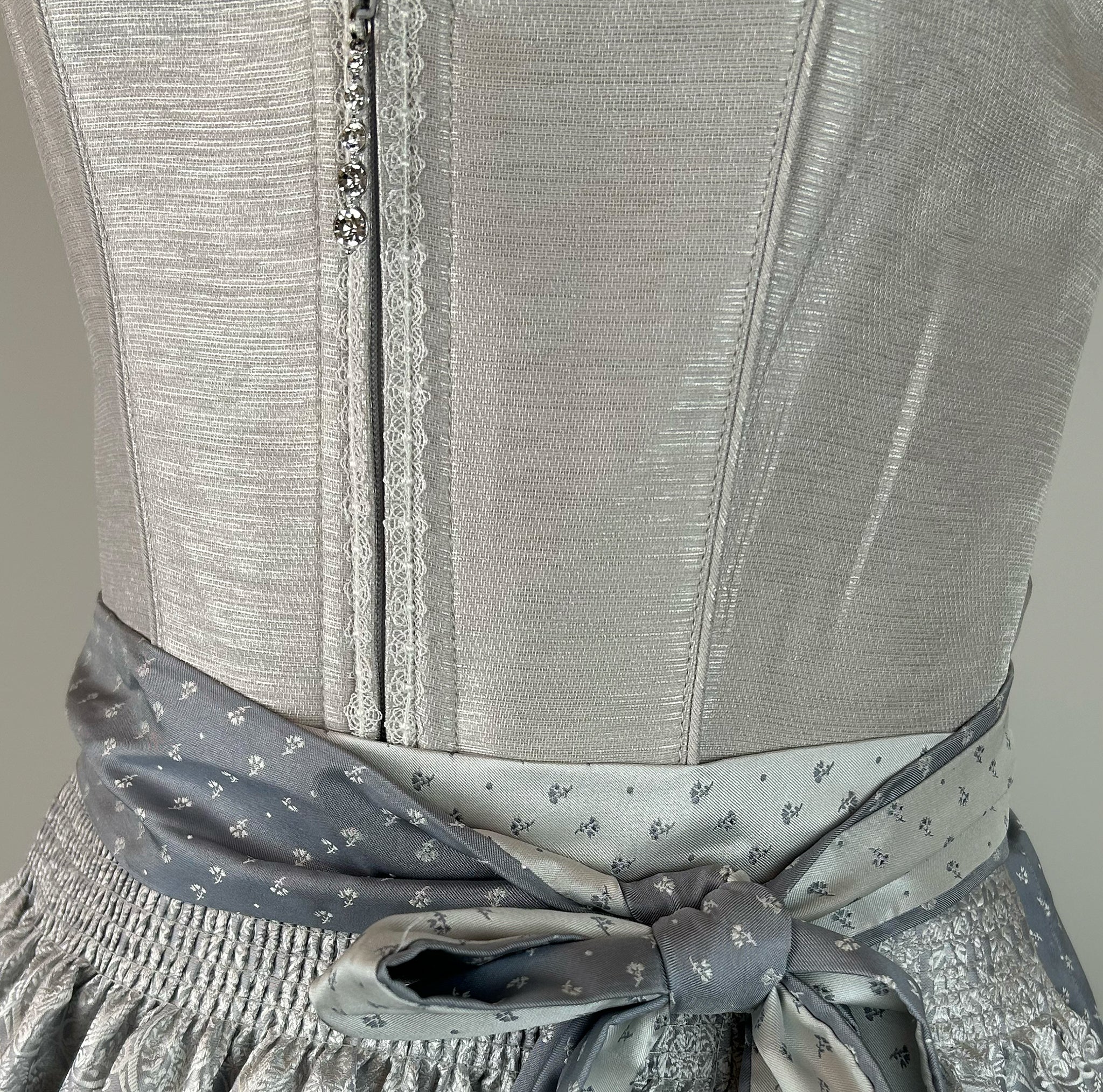 Elegant silver Krüger dirndl with lace details and patterned apron. Rent in Munich or online – perfect for Oktoberfest, weddings, and festive occasions.
