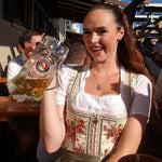 Woman in traditional cheeky Bavarian dress holding a large beer stein outdoors at Oktoberfest. Dirndl Dress ready to rent on Versatile OTM for Oktoberfest 