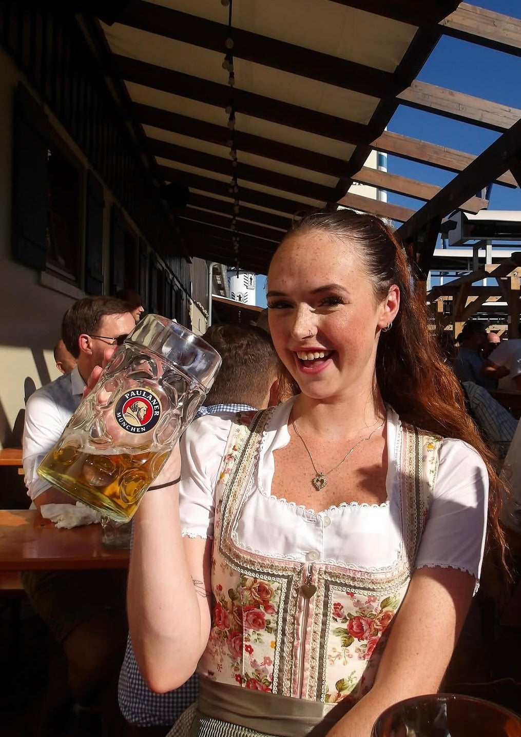 Woman in traditional cheeky Bavarian dress holding a large beer stein outdoors at Oktoberfest 
