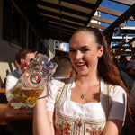 Woman in traditional cheeky Bavarian dress holding a large beer stein outdoors at Oktoberfest 