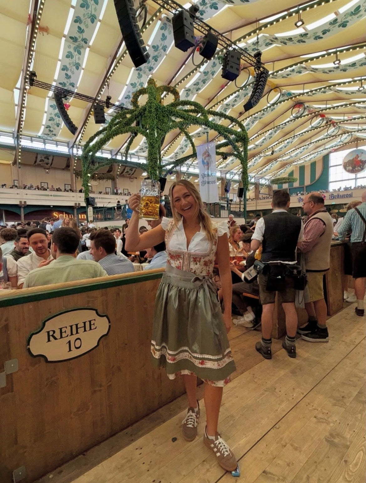 Woman in traditional Krüger Flower Dream Dirndl Bavarian in Oktoberfest Tent, holding a beer stein.
