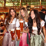 Three women in traditional German Dirndl at Oktoberfest in an Oktoberfest Tent holding beer mugs in a festive setting.