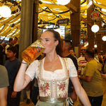 Woman in traditional Bavarian Dirndl holding a large beer stein in a festive Oktoberfest tent