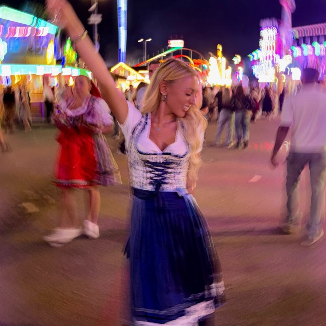 Girl wearing a rented Dirndl from Versatile OTM for Oktoberfest. Flowery Blue Dirndl for rent with Oktoberfest in the background 
