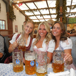 Three girls wearing rented Versatile OTM Dirndl for Oktoberfest in a beer tent with beer steens
