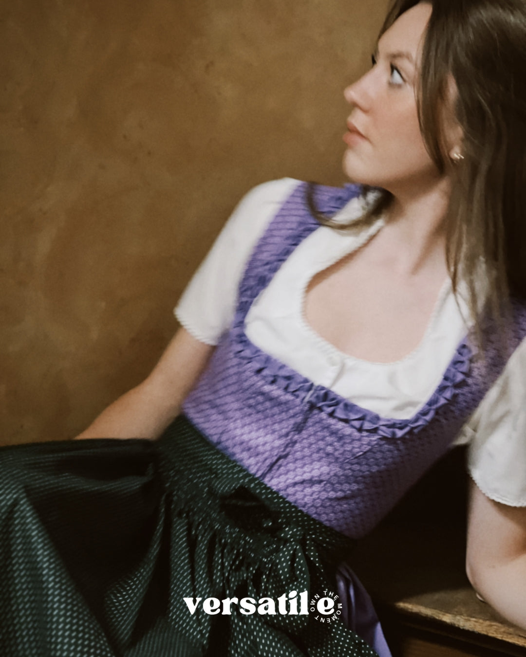 Woman wearing a purple green Dirndl Dress top over a white shirt with a brown background. Versatile Emilia Dirndl ready to rent 