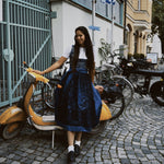 Woman in traditional Bavarian dress standing next to a scooter on a cobbled street with 'versatile' branding.