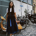 Woman in a blue dress standing on a street with bicycles and buildings in the background, featuring the brand 'versatile'.