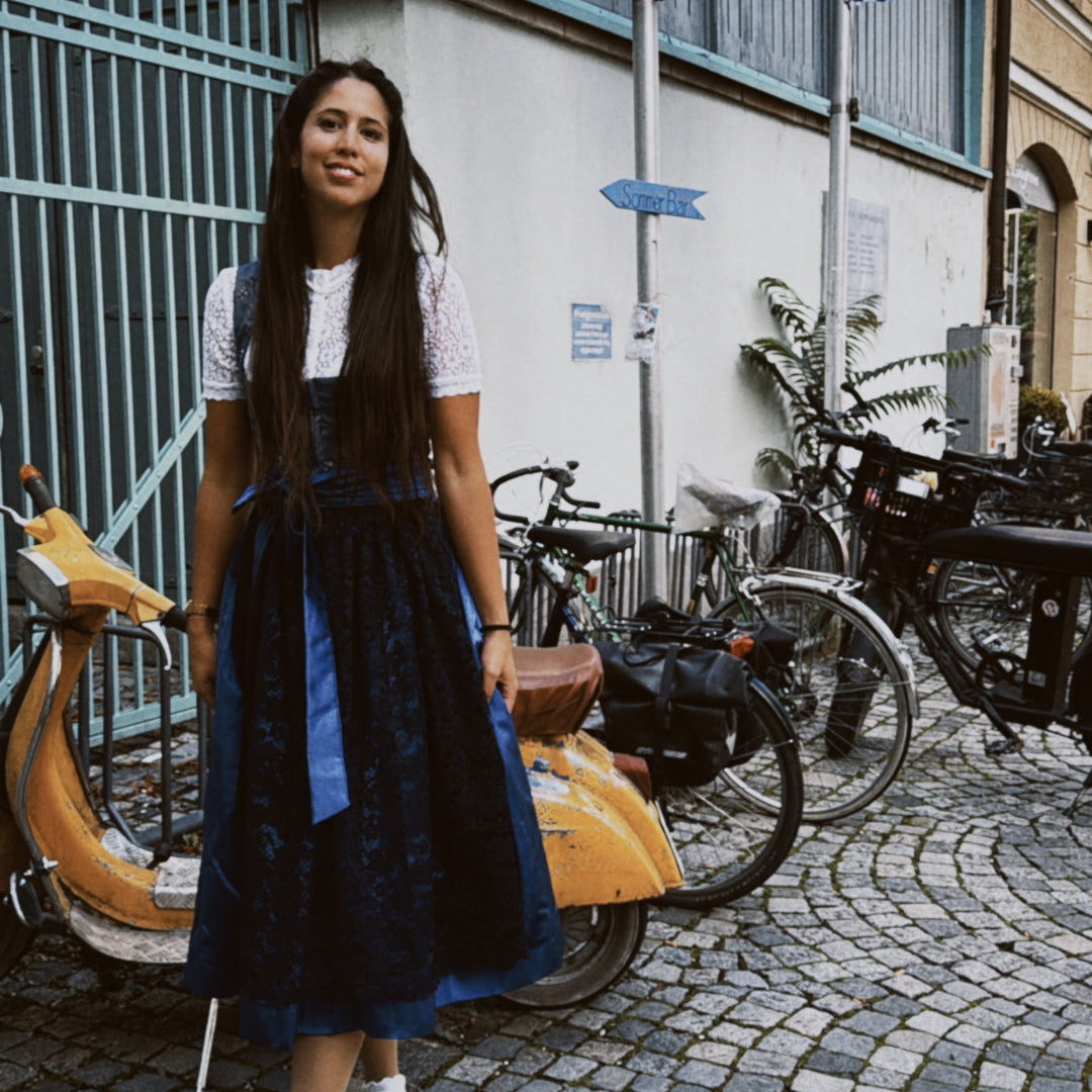 Woman in a blue dress standing on a street with bicycles and buildings in the background, featuring the brand 'versatile'.