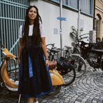 Woman in a blue dress standing on a street with bicycles and buildings in the background, featuring the brand 'versatile'.