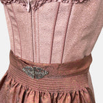 Detail: Short Krüger Dirndl Zafina with shimmering rose-pink bodice, heart-shaped neckline, and brown patterned apron – available to rent via Versatile.