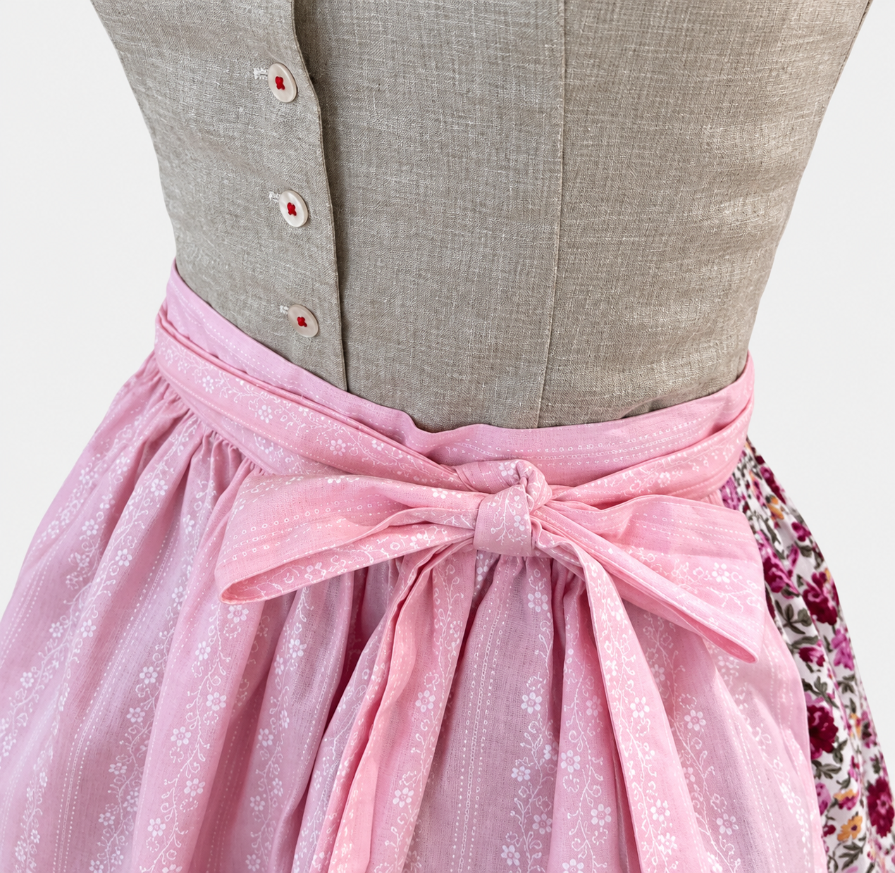Detail of Almsach Dirndl with textured grey beige buttoned bodice and pink apron bow with white floral pattern