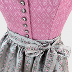 Detail of pink patterned Dirndl bodice with floral buttons and pale grey apron bow with pink rose medallions