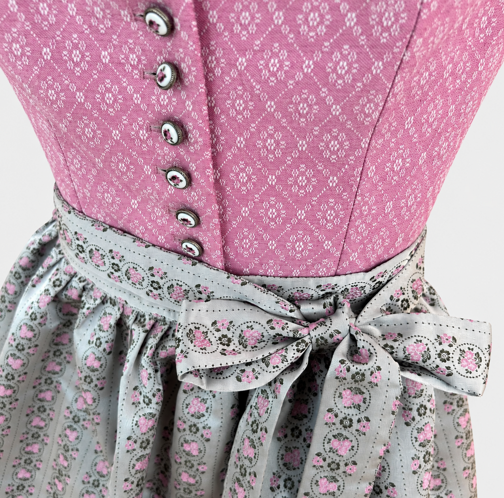 Detail of pink patterned Dirndl bodice with floral buttons and pale grey apron bow with pink rose medallions
