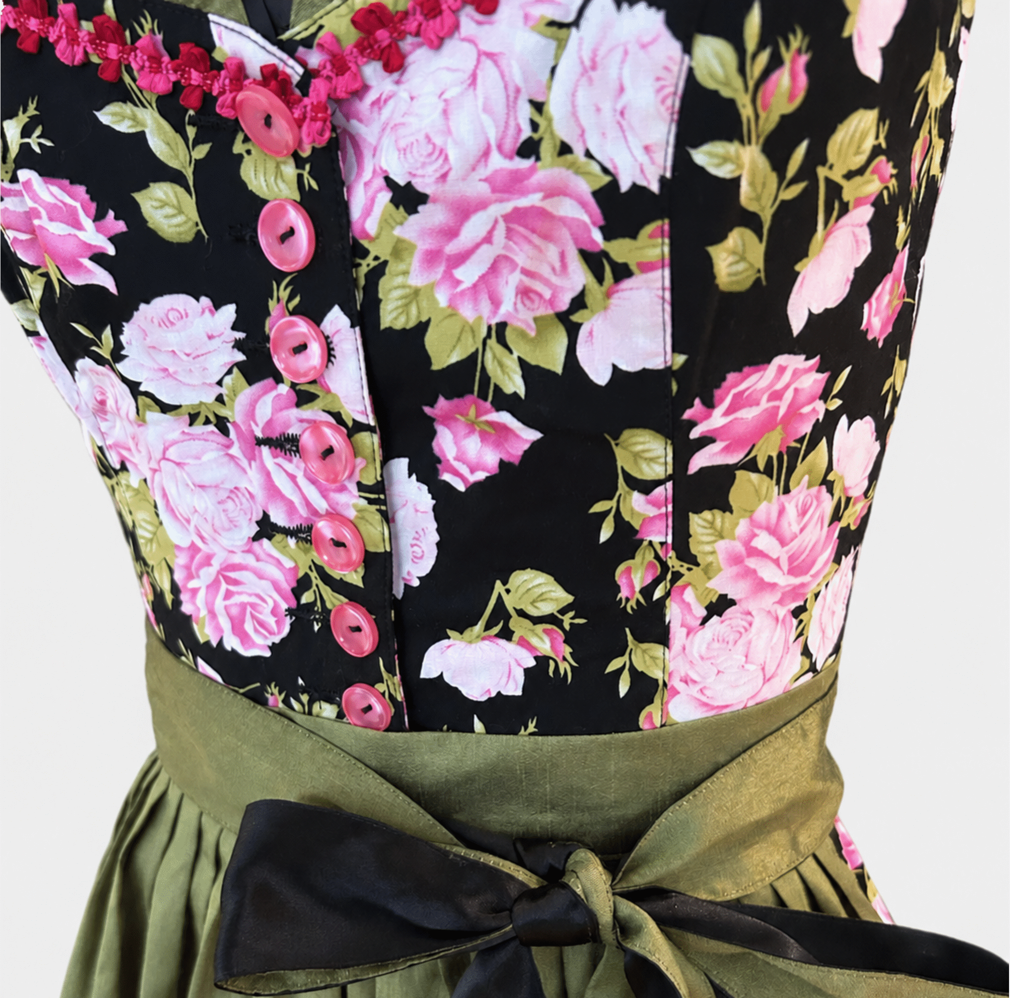 Close-up of a floral dirndl bodice with pink and white roses by Berwin & Wolff green leaves, pink buttons, a green satin waist belt, and a black bow.