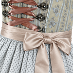 Detail of Krüger olive green Dirndl with ornamental bodice, taupe ribbon lacing, decorative hooks and bow over a patterned grey apron