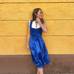 Alpine chic Ma.Le.Ma dirndl rental: deep royal blue with square-neck bodice, silk skirt, statement bow apron, and dotted underskirt—perfect for celebrating Oktoberfest in Munich.