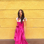 Rent Ma.Le.Ma artisanal fuchsia silk dirndl in Munich—handcrafted square-neck bodice, flowing skirt, tied bow apron; ideal for Oktoberfest.